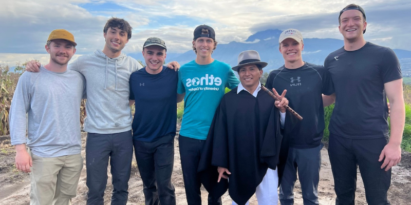 6 male students taking a photo with a native Ecuadorian man.